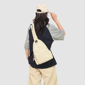 Macro detail of cream nylon crossbody chest bag showing round logo and zipper pockets