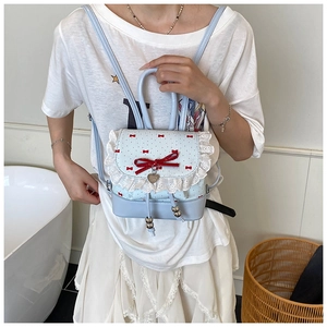 Detailed view of lace trim, red velvet bow, and heart pendant on a light blue backpack