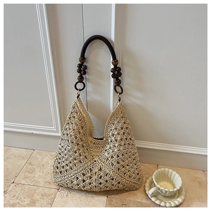 Detail of hand-woven straw tote with wooden beads and round handle on white wall