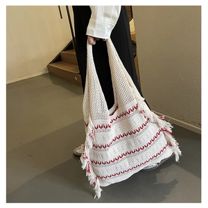Close-up of white knitted tote bag featuring red wavy patterns and fringe details