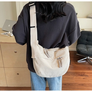 Close-up of off-white dumpling bag featuring woven rope zipper pulls and canvas strap