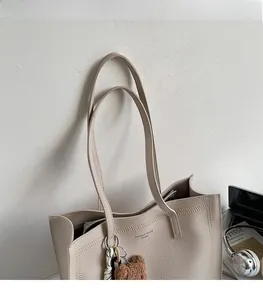 Close-up of beige tote bag with litchi grain texture and a brown plush bear charm