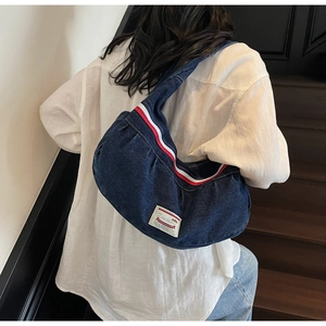 Close-up of a crescent-shaped dark blue denim shoulder bag with red-white decorative stripes