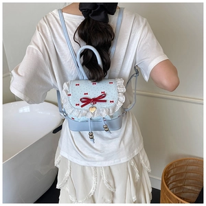 Detail view of light blue lace backpack featuring red ribbon bows and heart pendant