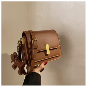 Detail view of brown leather square crossbody bag with gold buckle and dog charm