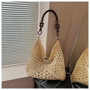 Detail of hand-woven straw tote with dark brown beaded handle in a natural setting