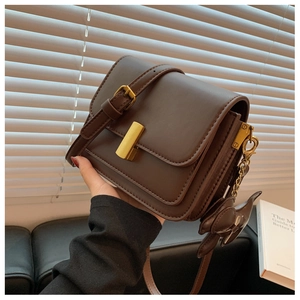 Brown leather crossbody bag detail featuring gold rectangular clasp and rabbit charm