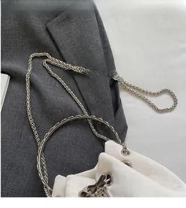 Detail of silver chain strap and circular metal handle on a white bucket bag