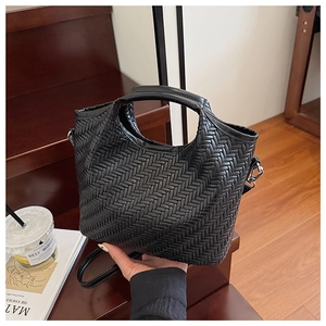Detail of a black woven leather tote bag featuring a textured pattern and detachable strap