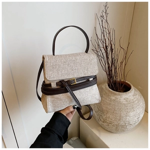 Détail d'un sac en toile beige avec poignées en cuir marron et boucles métalliques