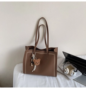 Detail of brown tote bag with pebble leather texture, plush bear charm, and chain strap
