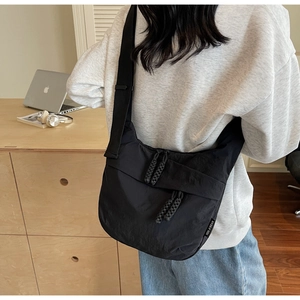 Detail shot of black nylon crossbody bag featuring woven zipper pulls and side brand label