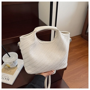 Detail of a creamy white woven tote bag with top handle and detachable shoulder strap
