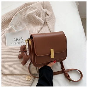 Macro shot of dark brown leather square bag with gold buckle and cute puppy charm detail