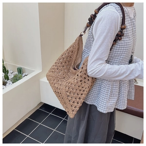 Detailed view of hollow crochet woven straw tote with decorative dark brown wood bead straps
