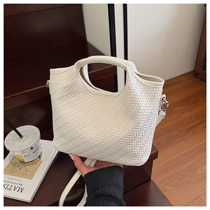 Detail view of a white woven handbag featuring a top handle and silver metal side hooks
