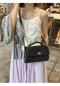 Detail of elegant black matte shoulder bag with silver turn-lock and leather handle