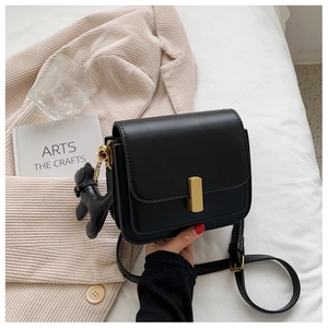 Detail of black faux leather crossbody bag featuring gold metal buckle and puppy charm
