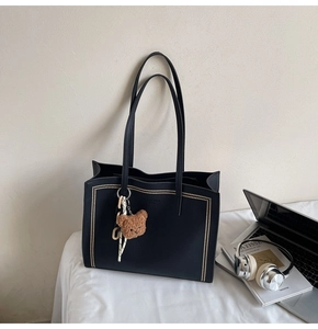 Detail of black pebbled leather tote bag with gold studs and a brown bear plush charm