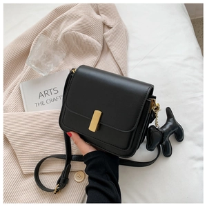 Detail of black crossbody bag with gold metal buckle and cute dog charm on beige fabric