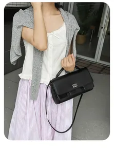 Detail of a chic black leather crossbody bag with silver rotating clasp worn by a model