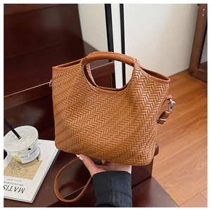 Detail of a brown woven leather bucket bag with a round handle and metal strap buckle
