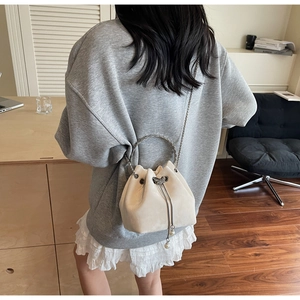 Detail of cream suede bucket bag with metal ring handle and pearl drawstring charms