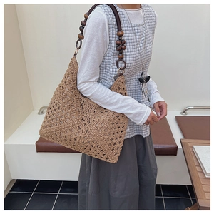 Detail of hand-woven straw tote with large brown wooden bead strap and hollow pattern