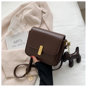 Detail of dark brown leather square bag with gold buckle and a cute puppy plush charm