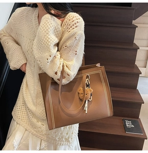 Brown tote bag with golden rivets and bear pendant shown on a casual female model