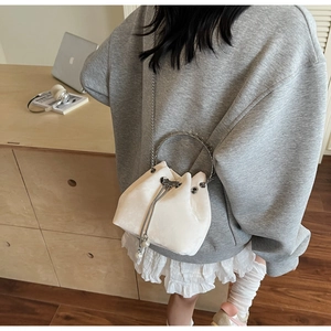 Detail of white plush bucket bag with drawstring closure and decorative pearl pendant