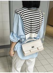 Minimalist beige rectangular handbag with silver metallic twist lock in a casual setting