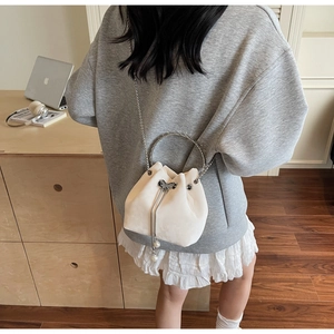 Detail of a beige bucket bag with metal ring handle, bow drawstring and pearl charms