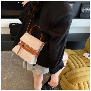 Détail d'un sac trapèze en tissu beige avec des lanières en cuir marron et boucle dorée
