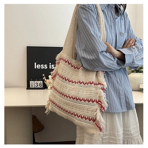 Detailed macro view of the cream knitted tote bag showing red heart pattern and fringe tassels