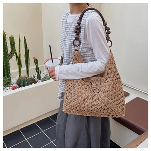 Detail of hand-woven hollow pattern and dark brown wooden bead shoulder strap on straw bag