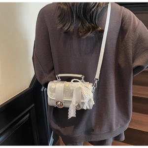 Silver cylinder crossbody bag with white lace bow and pearl chain worn by model