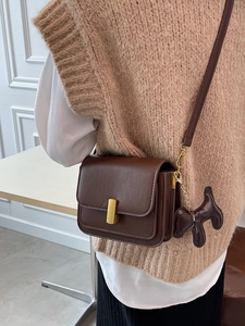 Dark brown leather shoulder bag with metal clasp and puppy charm shown on model