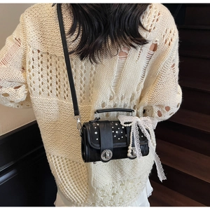Detail of black woven crossbody bag with lace bow, pearl charm, and shimmering rhinestones