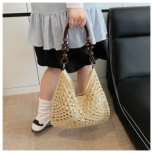Detail of hand-woven straw tote bag featuring a unique brown beaded wooden handle