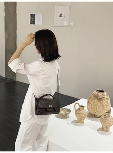 Detail of dark brown square crossbody bag with metal buckle on a model's shoulder