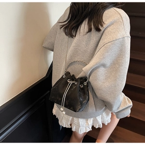 Detail of black drawstring bucket bag with metal rings, gold chain, and pearl accents