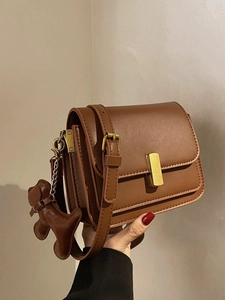 Brown leather rectangular crossbody bag with gold buckle and dog charm held by hand