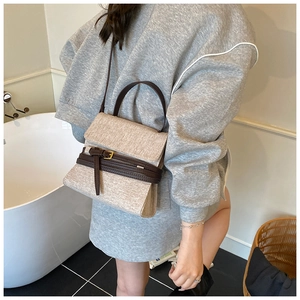 Détail de la texture tissée beige et bandoulière en cuir marron avec boucle dorée