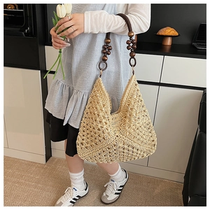 Detail of hand-woven straw tote bag with decorative dark brown wooden beads on shoulder strap