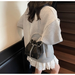 Detail of black textured bucket bag with silver chain strap and pearl drawstring charm