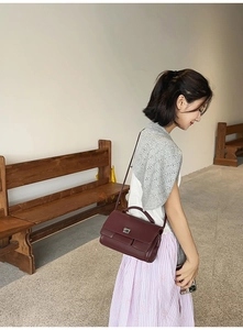 Elegant wine red square handbag with silver metal lock shown on shoulder by model