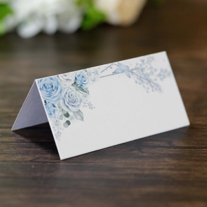 Close-up of white wedding place card with blue rose floral print on a wood surface