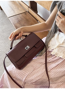 Deep burgundy leather handbag detail showing silver square twist lock and sleek top handle