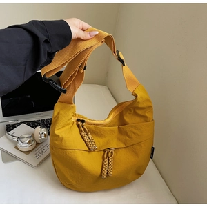 Detail of a ginger yellow nylon crossbody bag featuring a woven zipper pull and wide strap